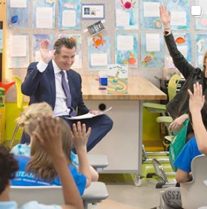 Governor Newsom raises his right hand while reading to children