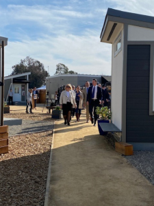 Governor Newsom walks with a tour of people as he visits tiny cabins at the Bridge Housing Community site in San Jose.