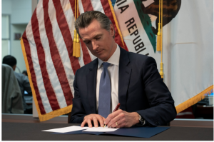 Governor Newsom sits at his desk and signs emergency legislation to fight COVID-19.