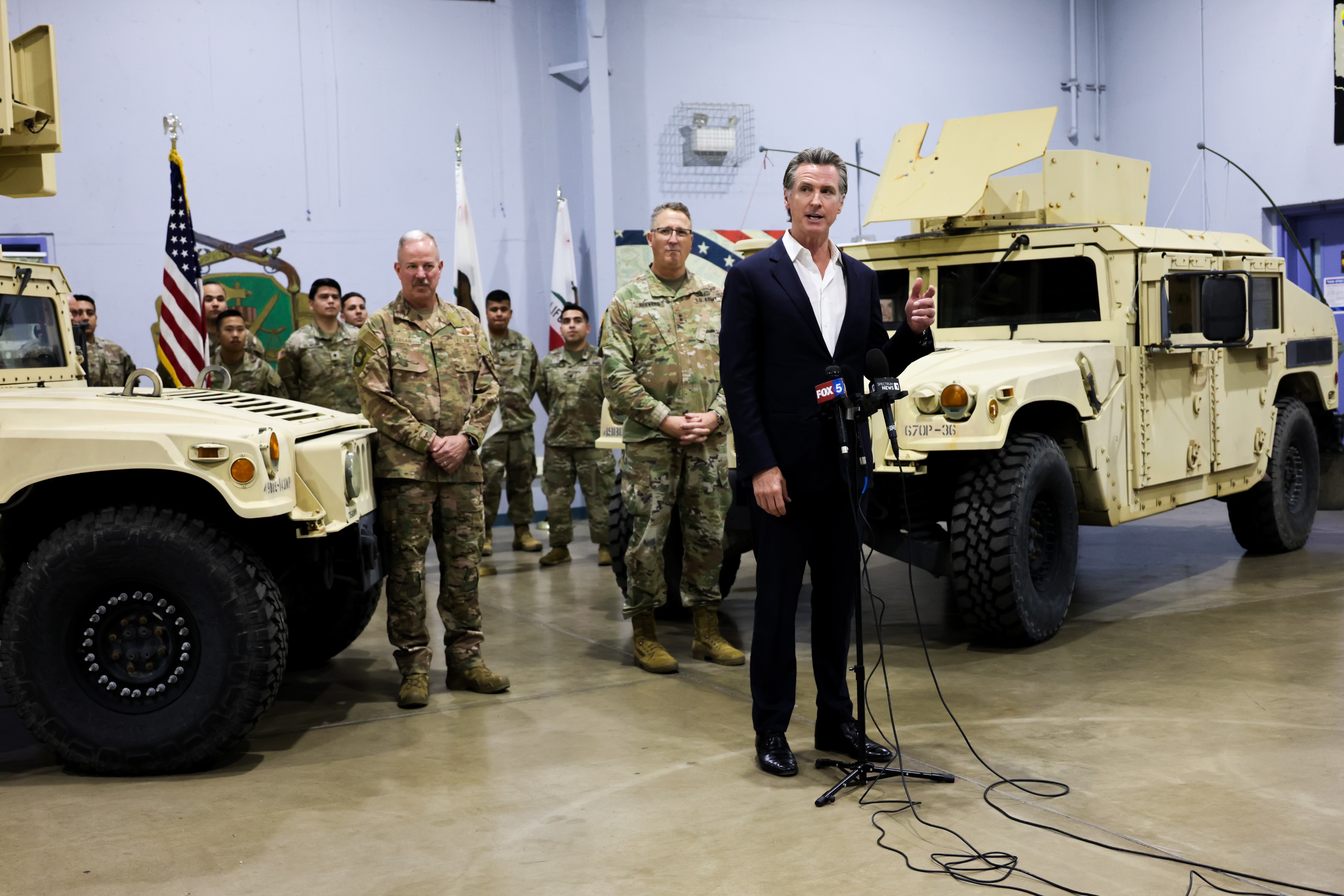 Governor Newsom standing in front of two military vehicles and a group of Cal Guard members