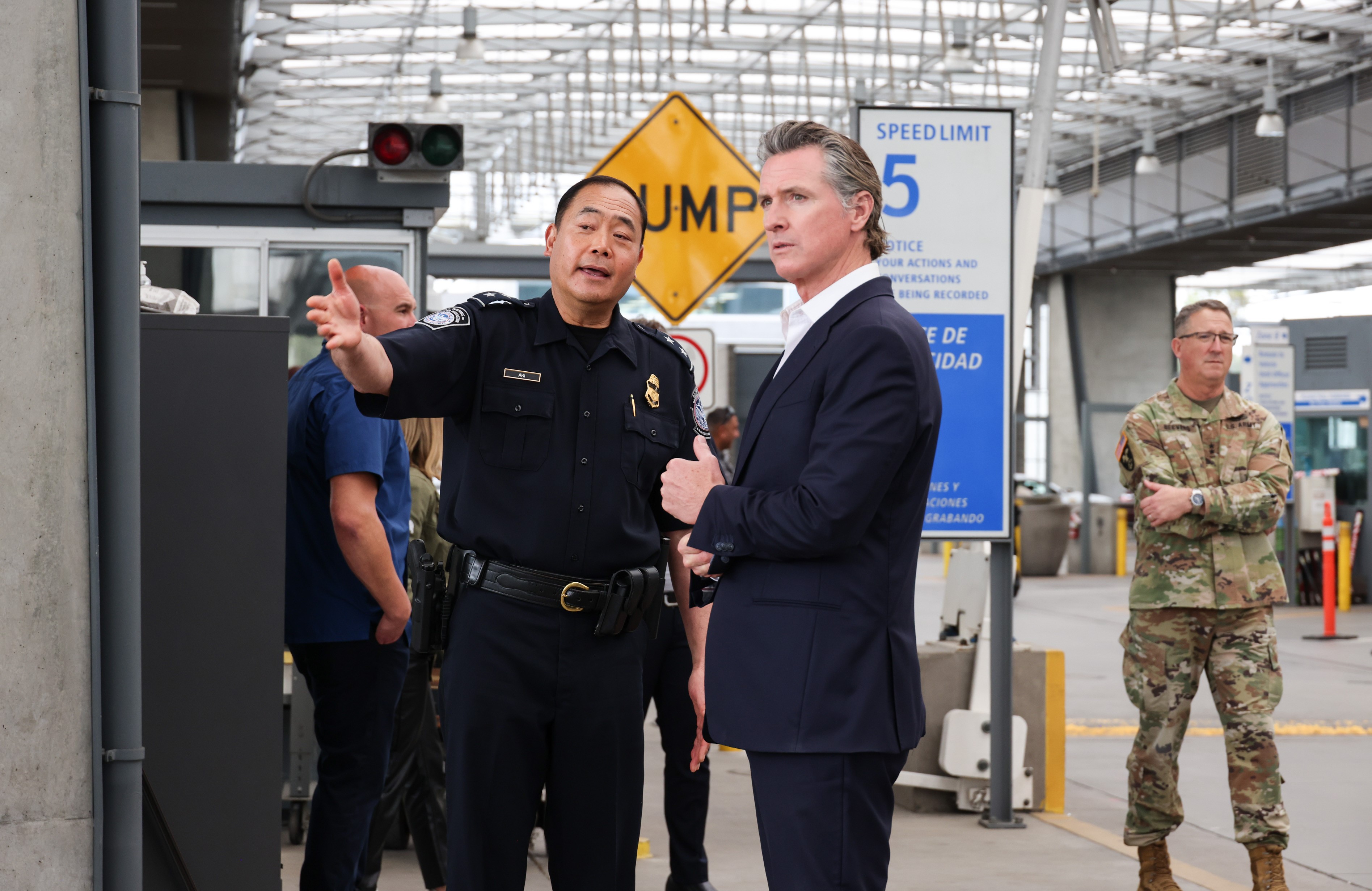 Governor Newsom looking off in distance while speaking with a uniformed officer in black clothing