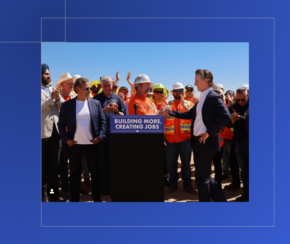 Governor reaching out to shake the hand of a construction worker with a crowd behind.