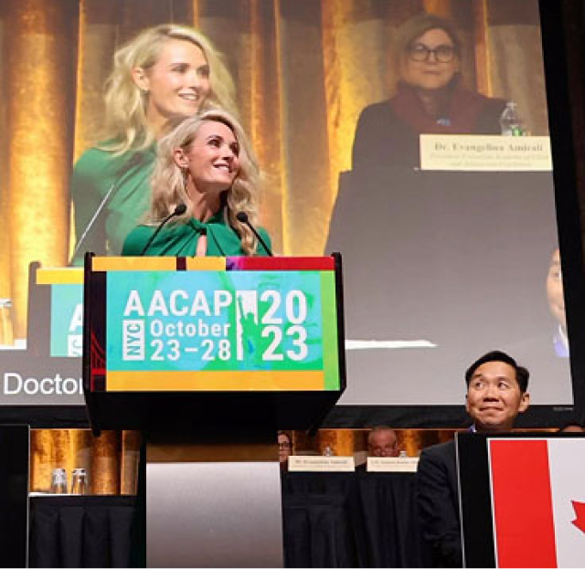 First Partner Jennifer Siebel Newsom smiles from behind a podium at the American Academy of Child & Adolescent Psychiatry event. The sign o the podium states AACAP. NYC. October 23 -28 2023.