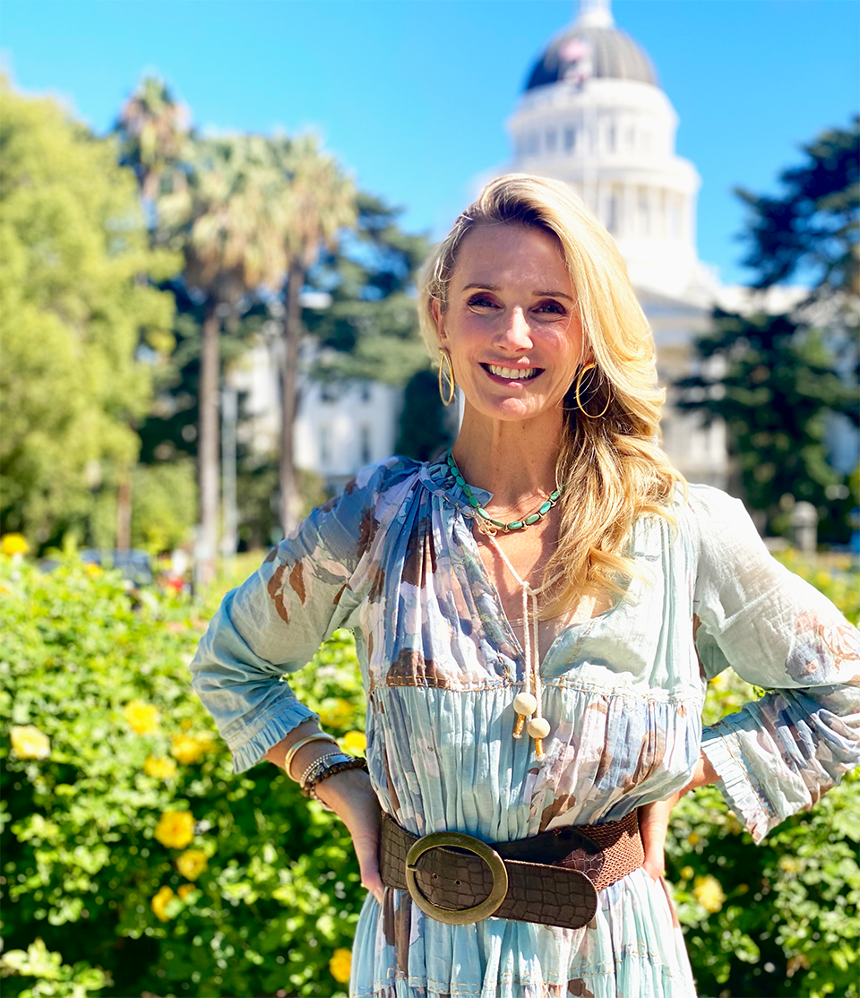 First Partner Jennifer Siebel Newsom smiles brightly in the sun in front of the state capitol.