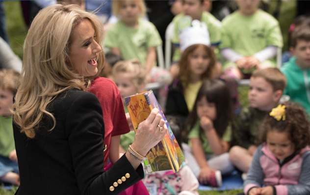 First Partner Jennifer Siebel Newsom smiling while reading a book to elementary school kids.