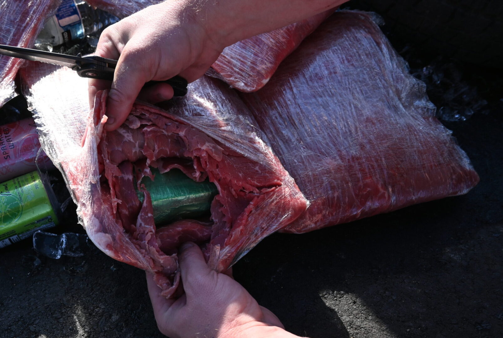 Image of hands holding open a package of meet containing a green package inside with fentanyl