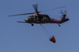 A photo of a Cal Guard firehawk helicopter with a bucket of water to fight wildfires