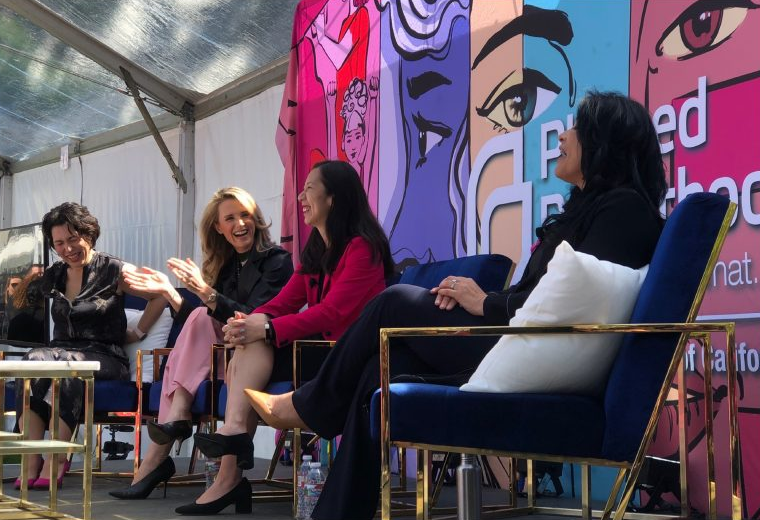 First Partner Jennifer Siebel Newsom sit on a panel with three other women, engaged in a discussion on stage. They are sitting in front of a banner for Planned Parenthood.