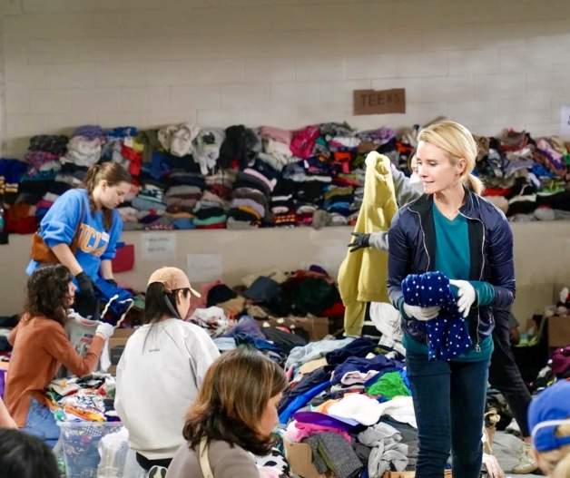 First Partner Jennifer Siebel Newsom, dressed in a red and blue floral dress, pose with four young women, smiling in front of a colorful mural staircase. The young women are wearing white flounced blouses and red embellished skirts with their hands on their hips.