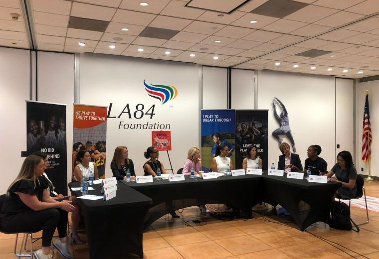 First Partner Jennifer Siebel Newsom and a group of women listen to a speak during a discussion. There is an LA84 Foundation banner.