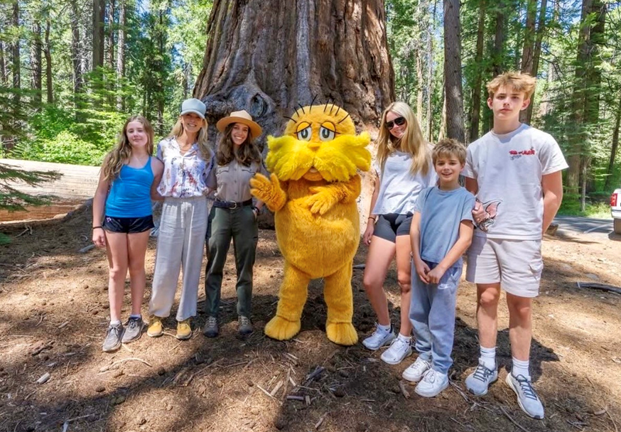 First Partner Jennifer Siebel Newsom and a large group of diverse women smiling and posing for a group photo in a room with elegant decor and red curtains.